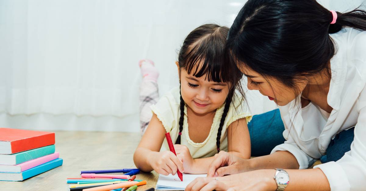 Mom and daughter happily looking at the page the daughter is scribbling.